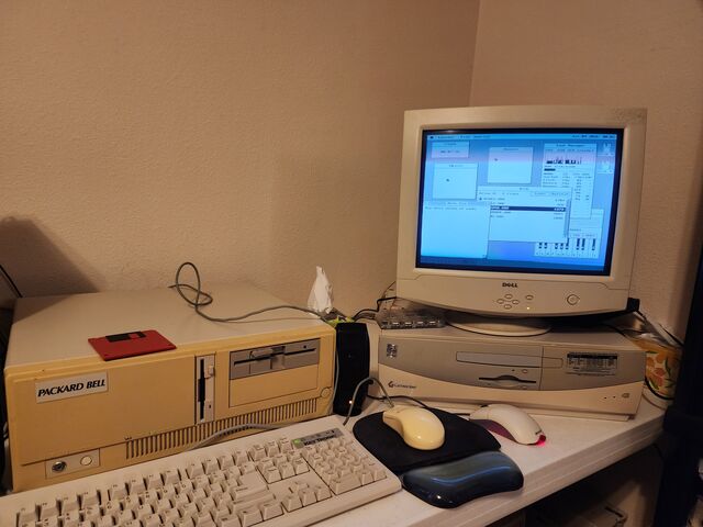 A corner of a desk with a beige Packard Bell desktop case and a Key Tronic keyboard on the left, and on the right a Gateway 2000 case with a Dell CRT on top of it displaying the os8088 desktop. Two mice and a mouse pad sit between them.