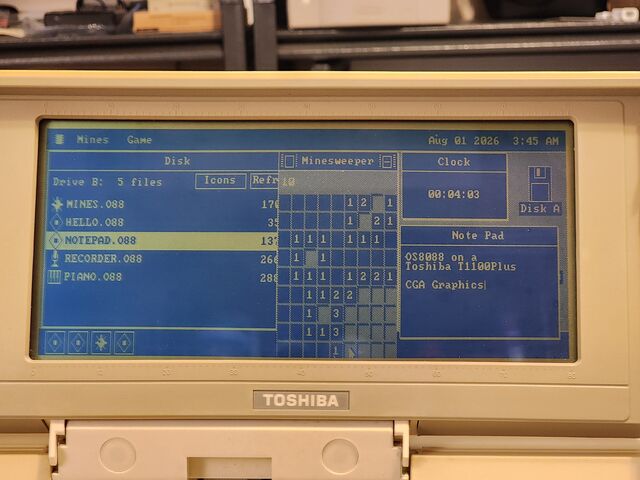 The Toshiba's blue LCD filling the frame. The menu bar reads Mines and Game on the left and Aug 01 2026 3:45 AM on the right. A Disk window lists MINES.O88, HELLO.O88, NOTEPAD.O88, RECORDER.O88 and PIANO.O88 with NOTEPAD highlighted; a Minesweeper board sits in the middle; a Clock reads 00:04:03; and a Note Pad reads OS8088 on a Toshiba T1100Plus, CGA Graphics.
